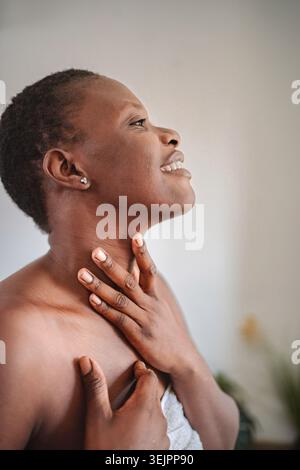 Young woman applying moisturizer on her neck after shower Stock Photo