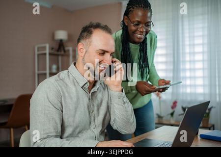 Multicultural couple working remotely from home, collaborating on digital devices Stock Photo