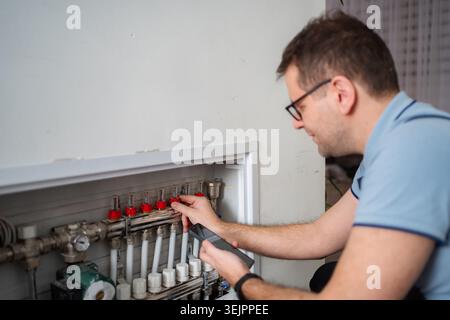 Technician adjusting a manifold valve for underfloor heating using a mobile phone Stock Photo