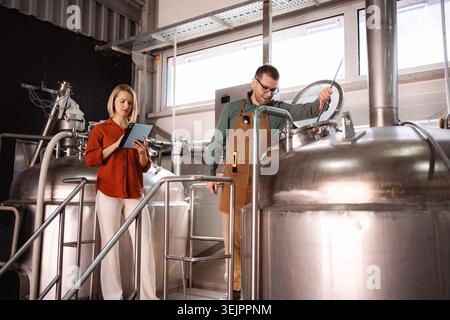 Colleagues collaborating in a microbrewery, checking beer fermentation and updating records Stock Photo