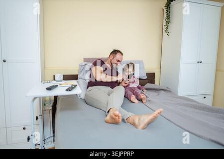 Father and daughter using smartphone in bed at home Stock Photo