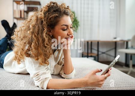 Young woman relaxing on bed using smartphone Stock Photo