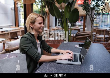 Woman working on laptop and smiling in cafe Stock Photo