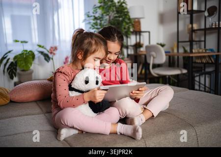Sisters sharing digital tablet at home learning and playing Stock Photo