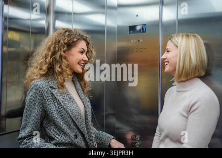 Two female friends having fun talking in elevator Stock Photo