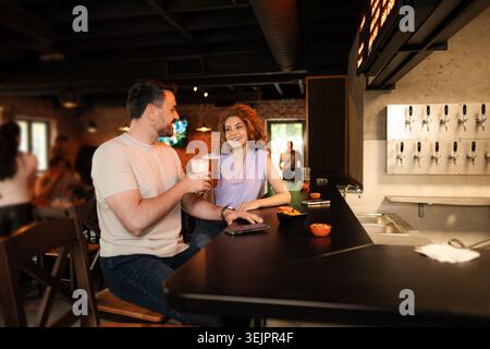 Couple drinking beer and eating snacks at the counter in a pub Stock Photo