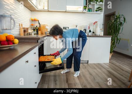 Young woman baking pizza in modern kitchen oven Stock Photo