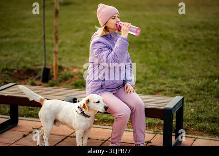 Woman drinking water with dog in park Stock Photo
