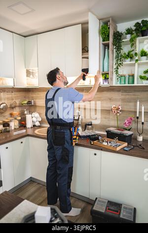 Handyman installing kitchen cabinets using electric screwdriver Stock Photo