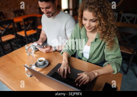 Young woman working on laptop while man using smartphone in cafe Stock Photo