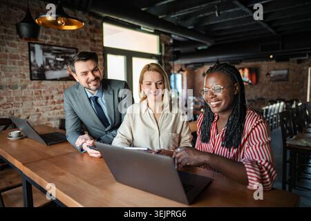 Diverse business people working together on a laptop in a cafe Stock Photo