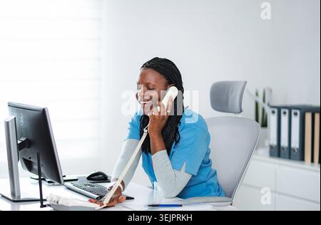 Black female medical receptionist talking on telephone at office Stock Photo