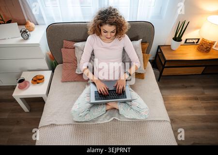 Young woman working remotely on laptop in bed Stock Photo