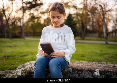 Girl sitting in park using mobile phone Stock Photo