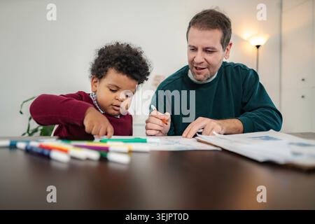 Father and son sitting at table drawing together Stock Photo