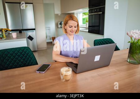 Woman working on laptop in modern kitchen workspace Stock Photo
