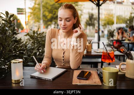 Woman using a stylus on a digital tablet at a cafe table with a drink Stock Photo