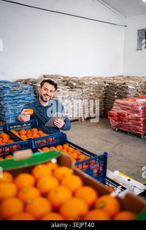 Worker checking fresh oranges with digital tablet in warehouse Stock Photo