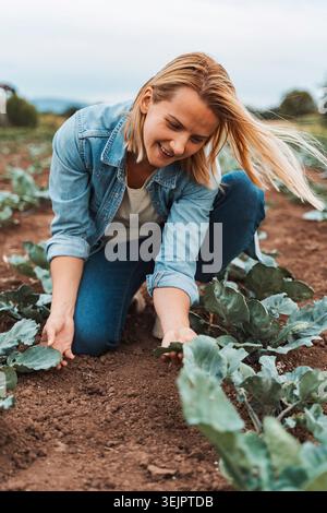 Young farmer woman checking vegetables growing in field Stock Photo