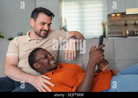 Interracial couple relaxing on sofa using smartphone at home Stock Photo