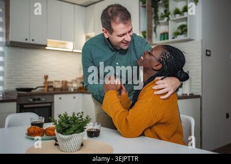 Interracial couple sharing happy morning moments in kitchen Stock Photo