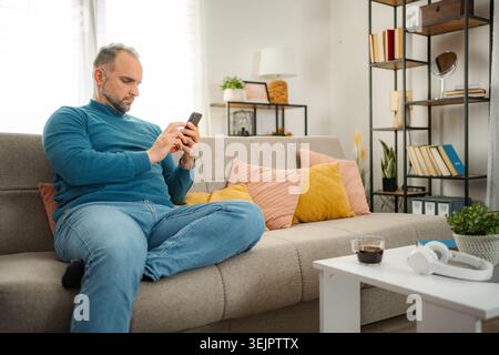 Man relaxing on sofa using smartphone at home Stock Photo