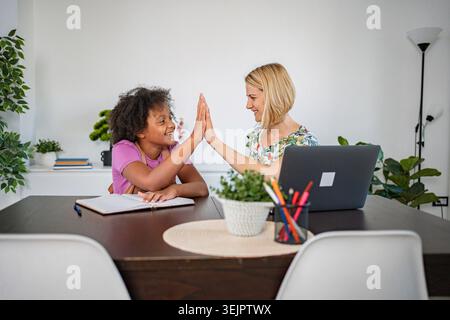 Mother and daughter giving high five while doing homework at home Stock Photo