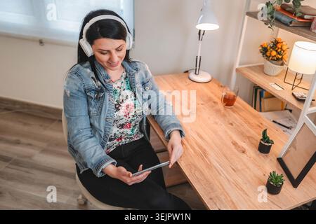 Smiling female freelancer working from home and listening to music with headphones Stock Photo