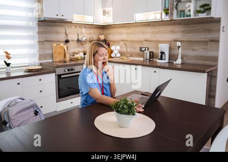 Tired Female Doctor Yawning While Working From Home Stock Photo
