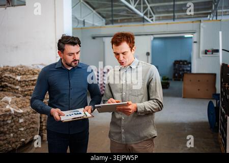 Warehouse managers analyzing data on digital tablet and clipboard Stock Photo