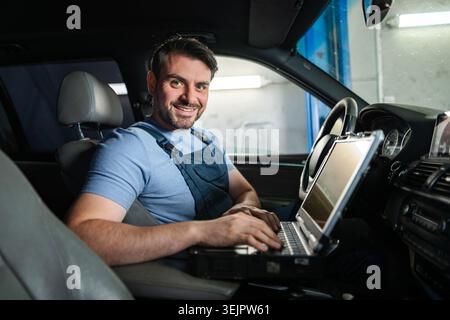 Car mechanic using laptop for computer diagnostics inside car in auto repair shop Stock Photo