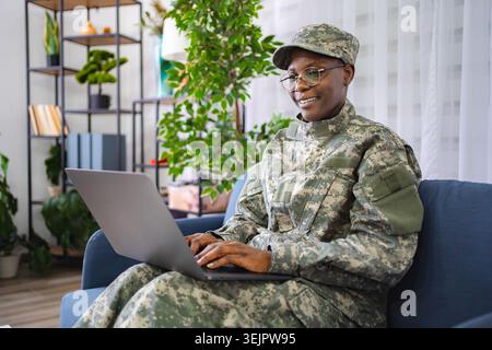 Smiling female soldier using laptop at home Stock Photo