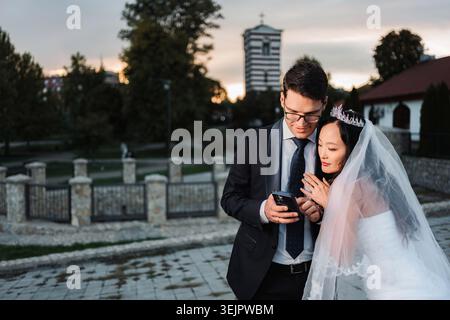 Interracial wedding couple looking at smartphone together outdoors Stock Photo