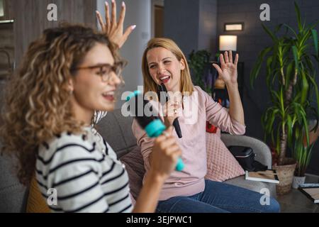 Two female friends having fun singing with hairbrushes as microphones at home Stock Photo