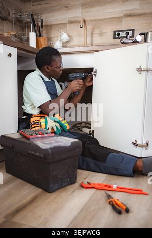 Handyman using cordless drill to install cabinet door in a modern kitchen Stock Photo