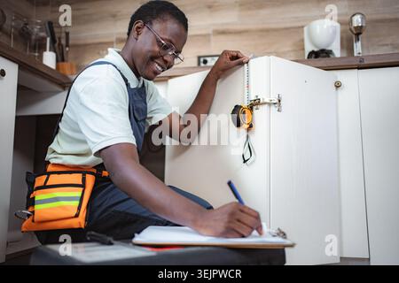 Female Carpenter Taking Measurements of Kitchen Cabinets and Writing Notes Stock Photo