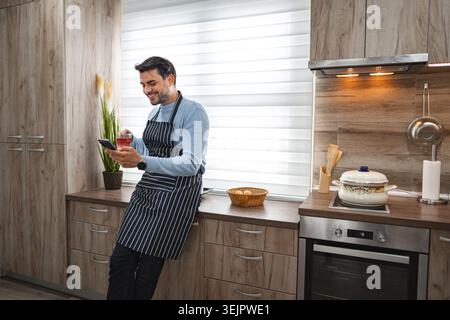 Man in the kitchen using mobile phone while waiting for meal to cook Stock Photo