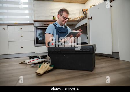 Handyman using digital tablet while repairing kitchen cabinet Stock Photo