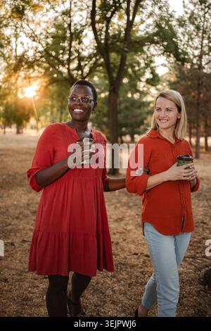 Two smiling friends walking and talking in a park at sunset Stock Photo