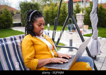 Woman working remotely on laptop wearing headphones in garden Stock Photo