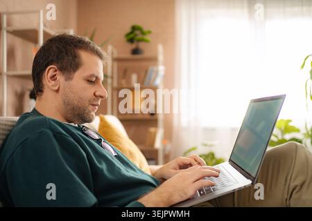 Man typing on laptop working from home comfortably Stock Photo