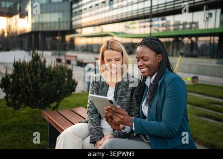 Diverse businesswomen collaborating outdoors with digital tablet Stock Photo