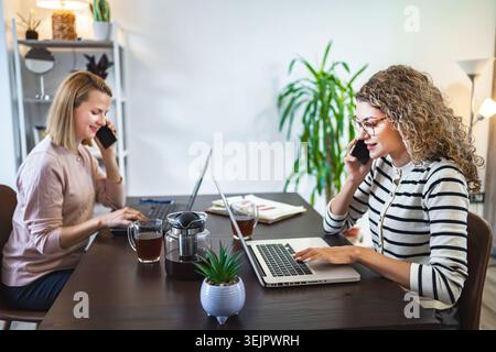 Two businesswoman working at a desk on laptop and talking on a phone call Stock Photo