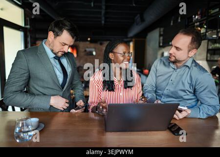 Diverse business team collaborating on laptop at a cafe bar Stock Photo
