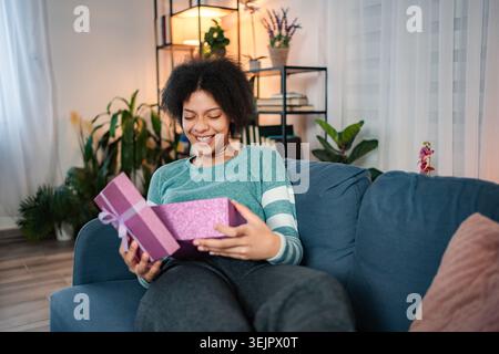Young woman receiving surprise while opening gift box at home Stock Photo