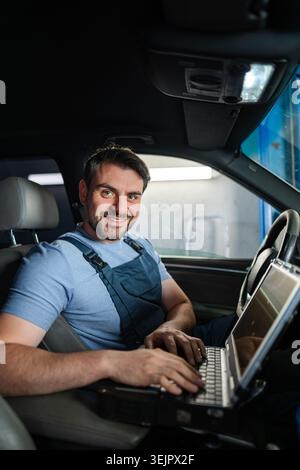 Smiling car mechanic using laptop for diagnostics inside a car Stock Photo