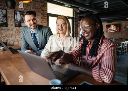Diverse business professionals discussing work using laptop in cafe Stock Photo