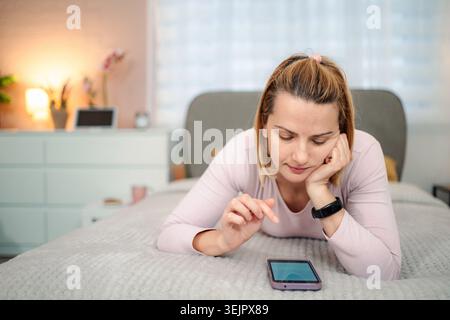 Woman lying on bed using smartphone at home Stock Photo
