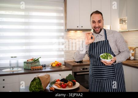 Man chef showing OK sign holding bowl of brussels sprouts Stock Photo