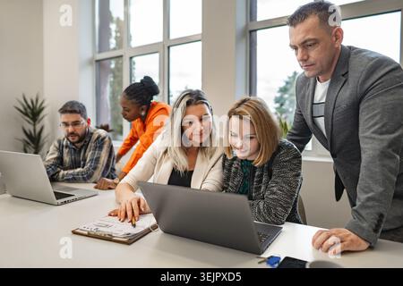 A diverse group of individuals gathered around a laptop, focused on its screen. They appear engaged and attentive, possibly discussing or collaboratin Stock Photo